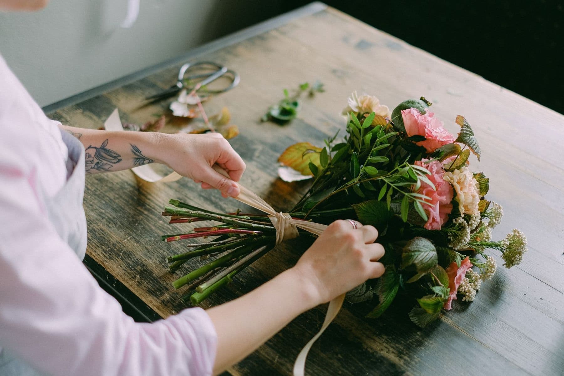Hands tying a bouquet of pink roses with string