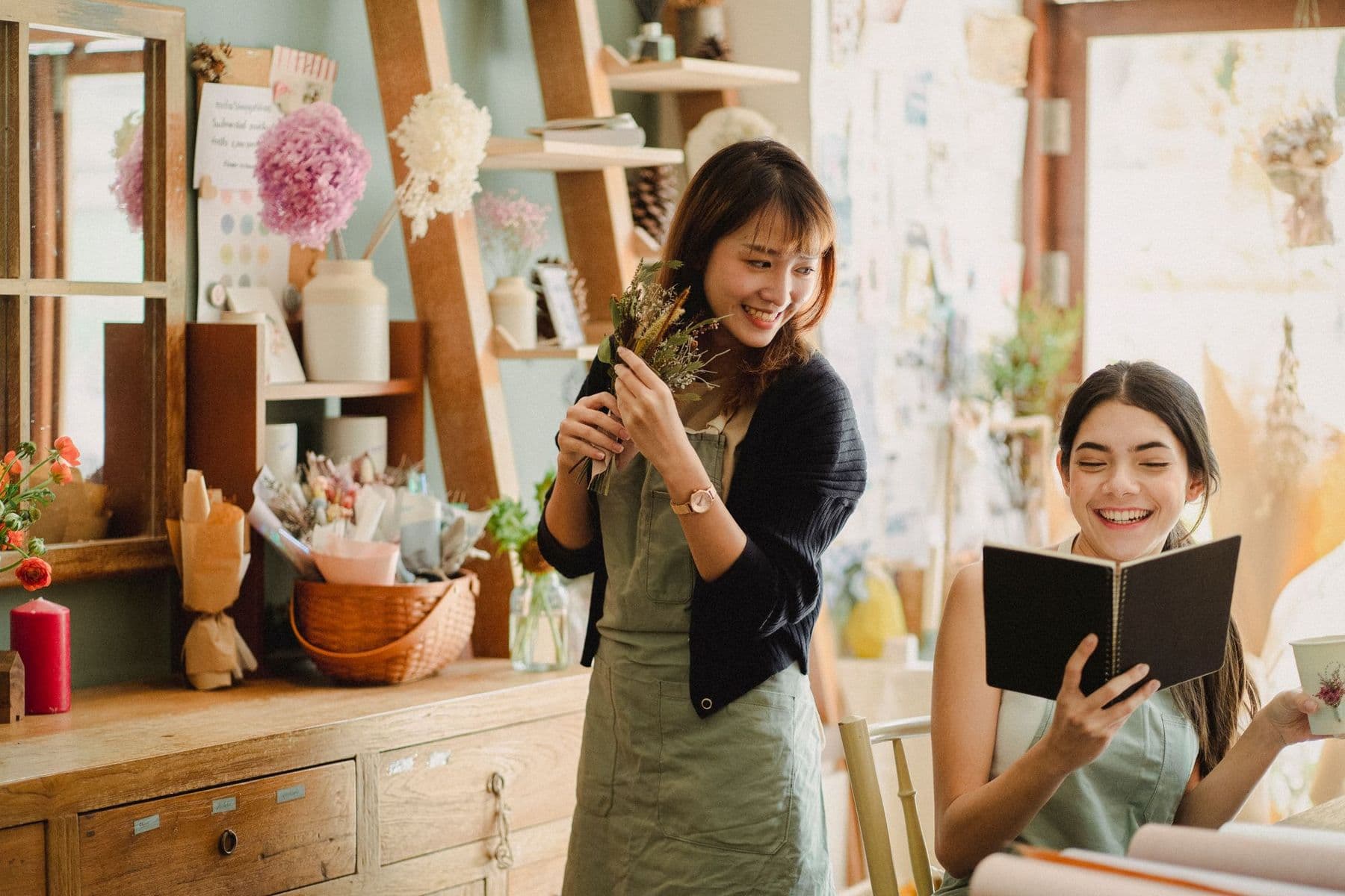 Two florists laughing together behind the shop counter