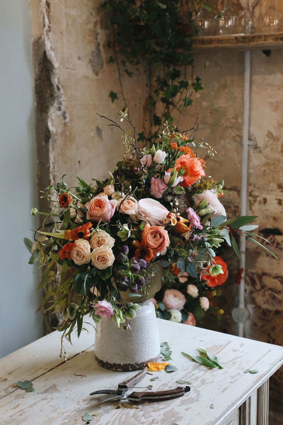 Peach roses, dahlias and coral blooms arranged in a stone urn on a florist's workbench